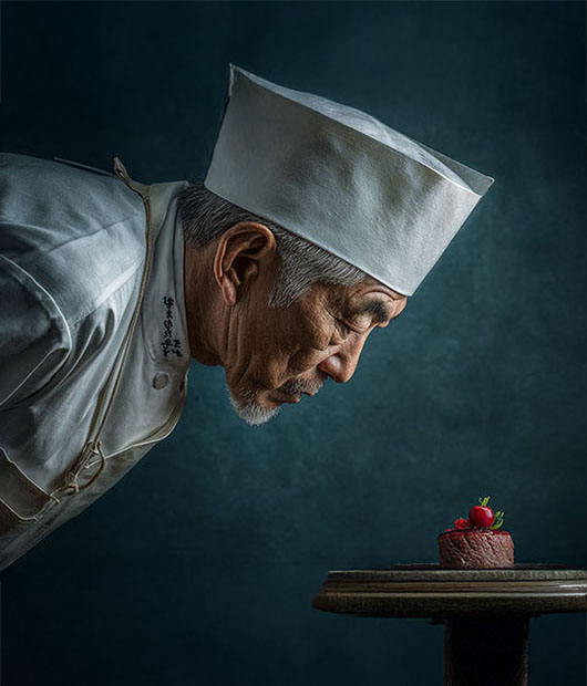 A pastry chef leaning in to inspect a small cake