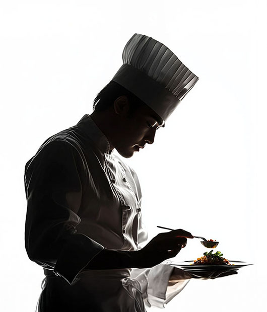 A chef in silhouette plating a dish